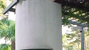 Ein Beton-Grill für den Außenbereich mit einem Metallrost, umgeben von einem Garten mit verschiedenen Pflanzen und einer gepflasterten Fläche.