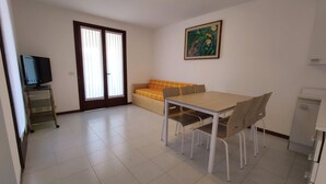 Ein Zimmer mit Esstisch, Stühlen, einer Couch, einem Fernseher auf einem Wagen und einer Küchenzeile.
