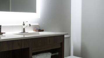 Un baño moderno con un lavamanos blanco, tocador de madera oscura, inodoro blanco y un espejo grande.