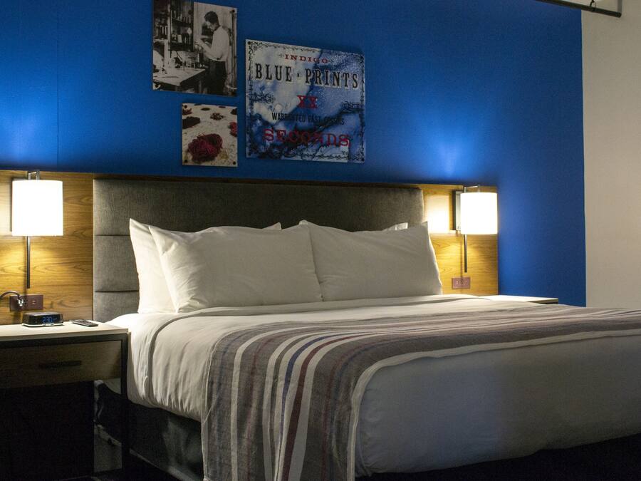 A hotel room with a large bed, two bedside lamps, a nightstand, and a wall with framed pictures.