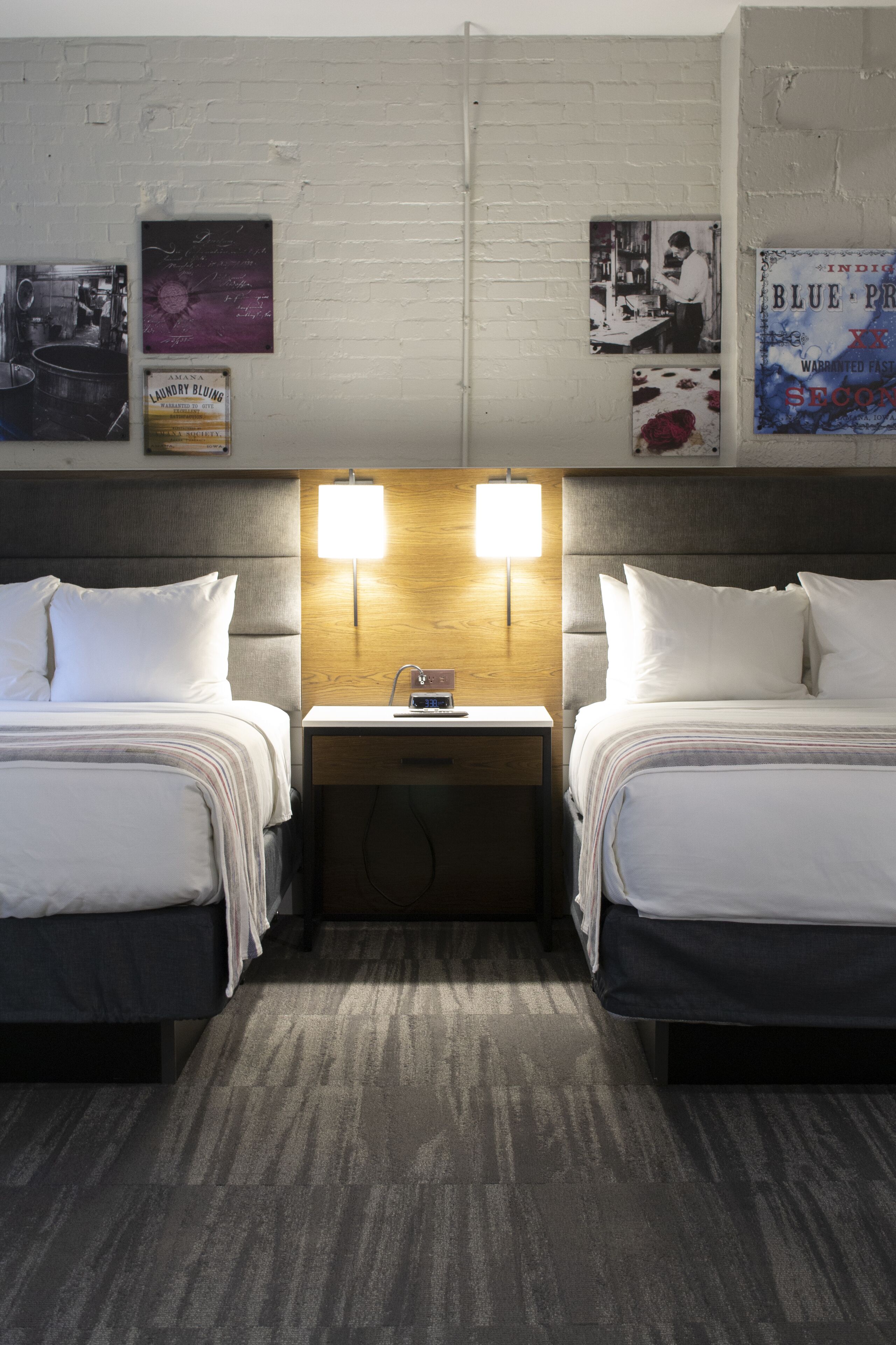 A hotel room with two beds, a nightstand with a lamp, and a wall with framed pictures.