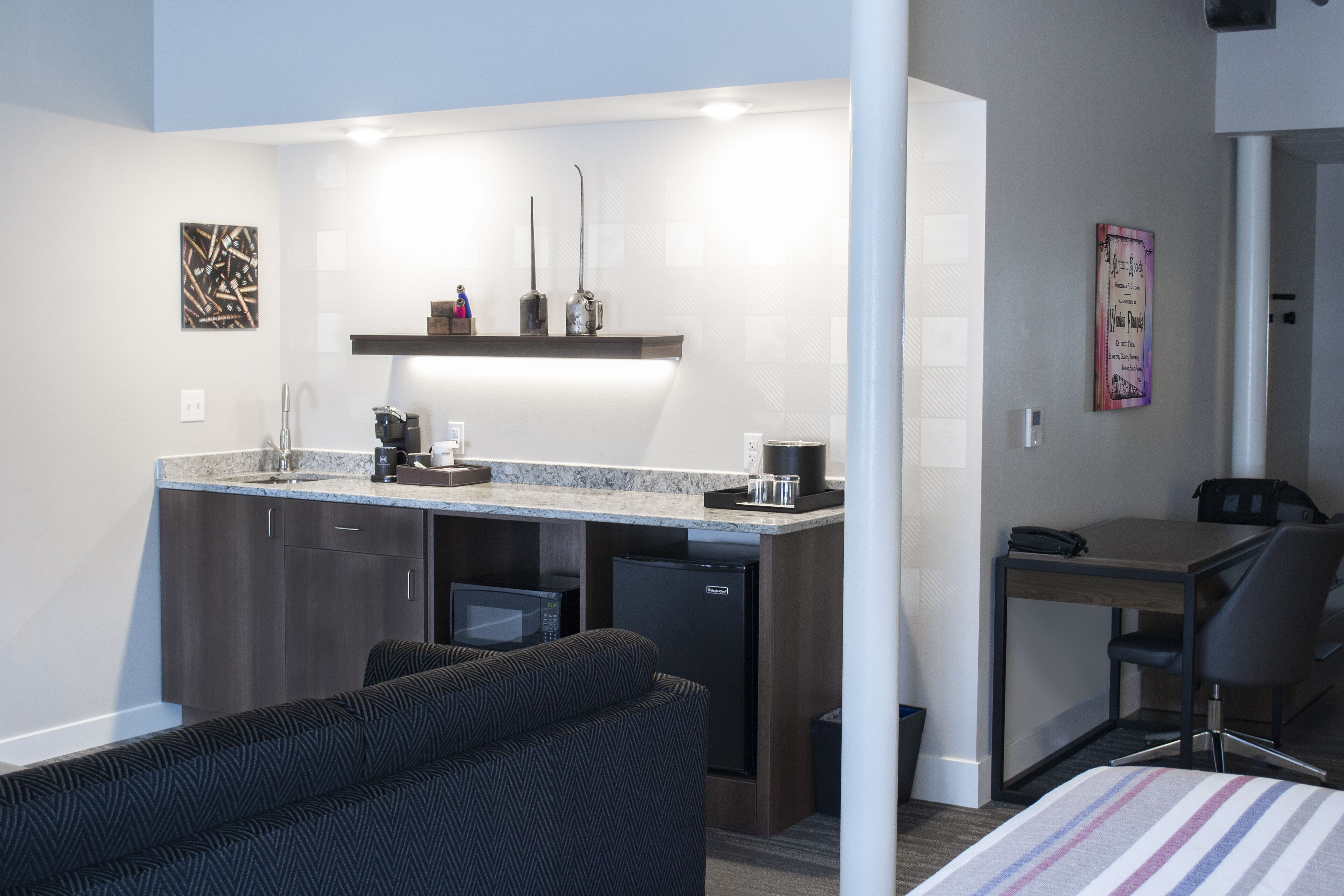 Una habitación de hotel compacta con kitchenette, un sofá, un escritorio pequeño y una cama.
