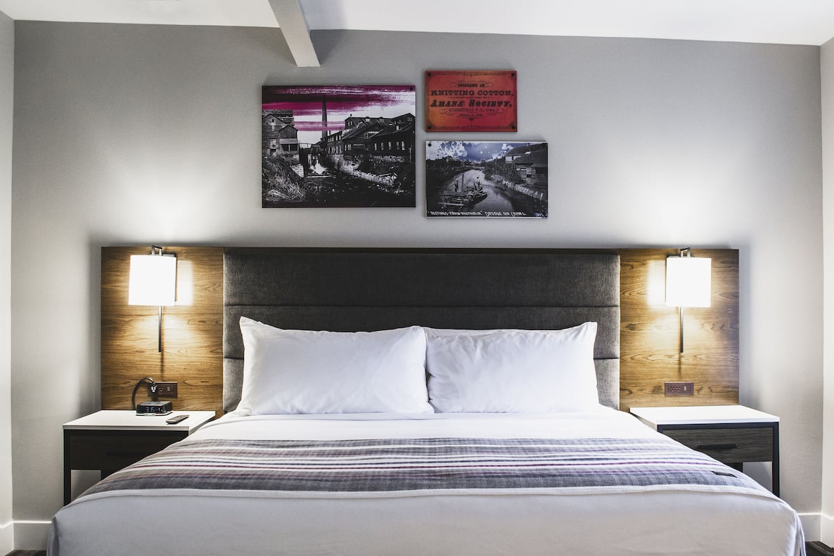 Une chambre d’hôtel avec un grand lit, deux tables de chevet avec des lampes et trois tableaux encadrés au mur.