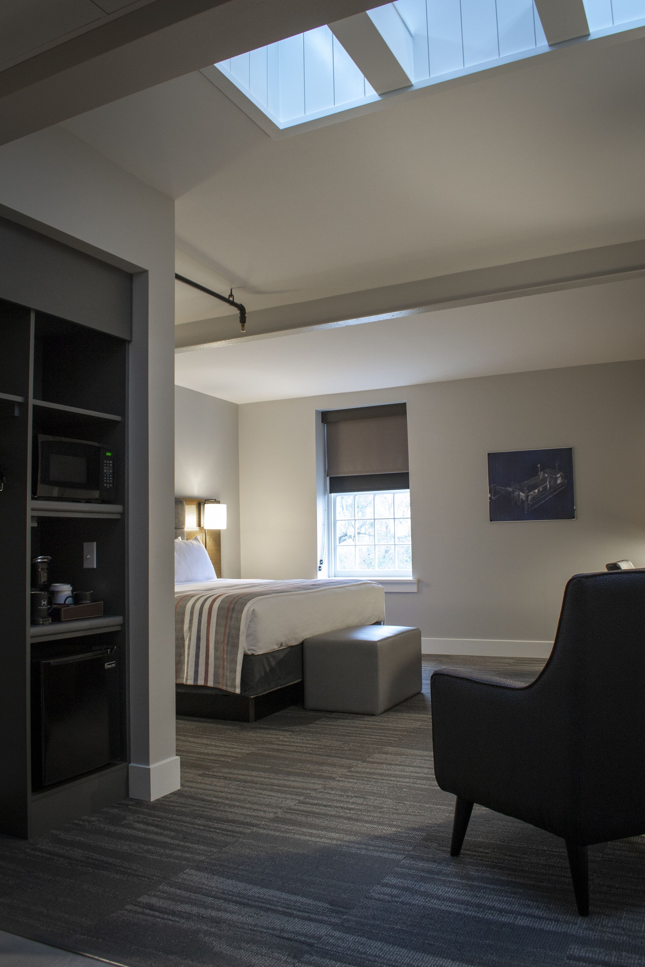 A modern hotel room with a skylight, a bed, a desk, and a chair.