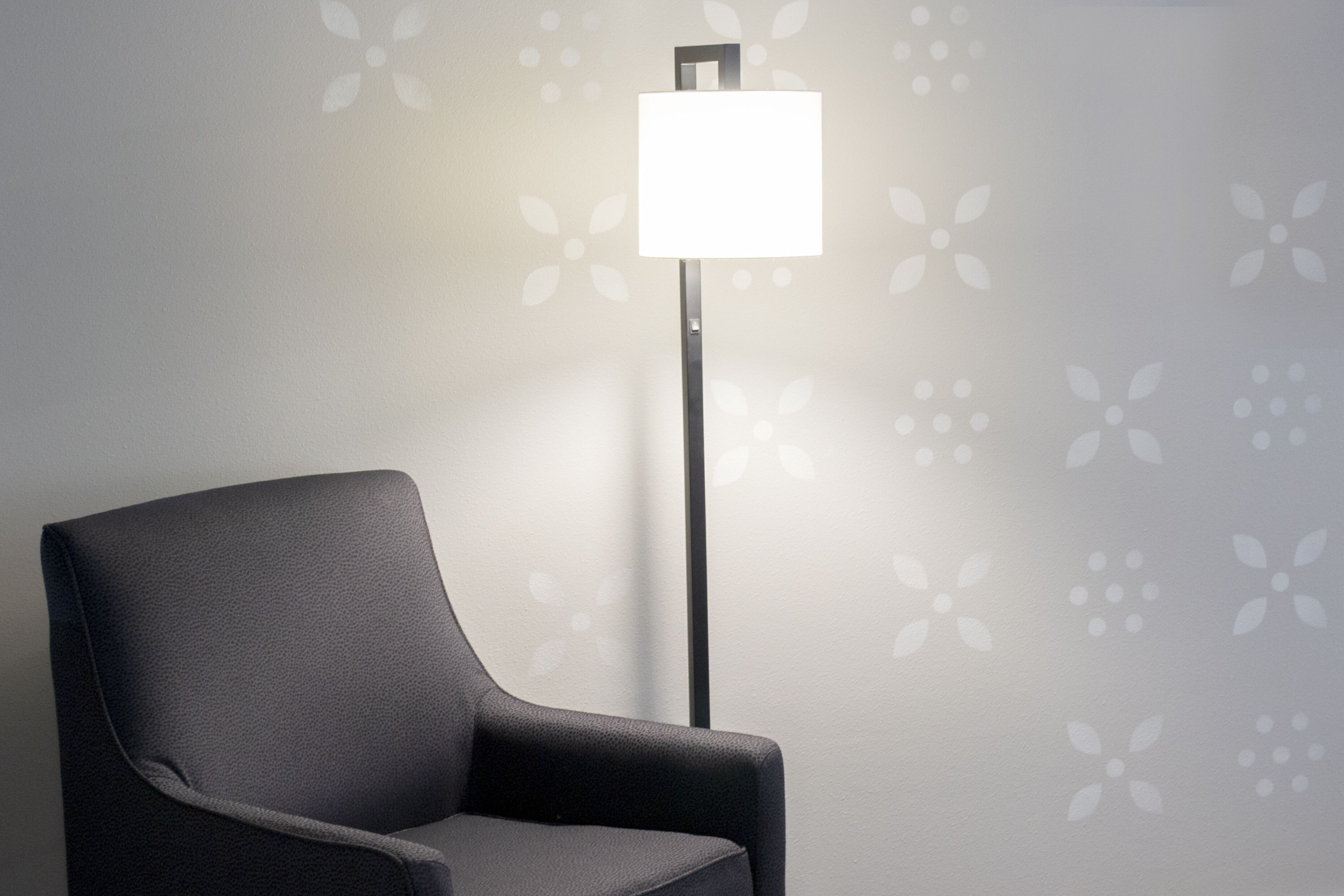 Ein moderner Sessel und eine Stehlampe vor einer blumengemusterten Wand.