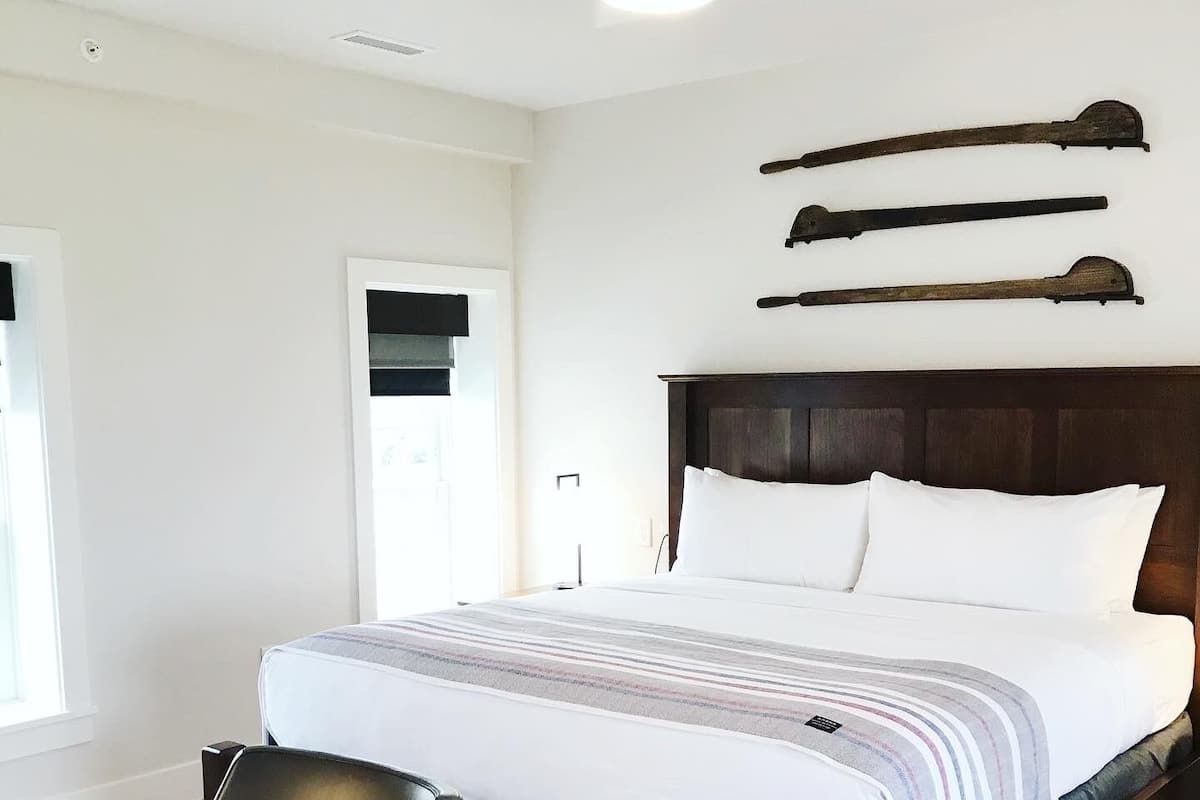 Une chambre à coucher avec un lit en bois, du linge de lit blanc, une table de chevet en bois, une chaise et un ventilateur de plafond.