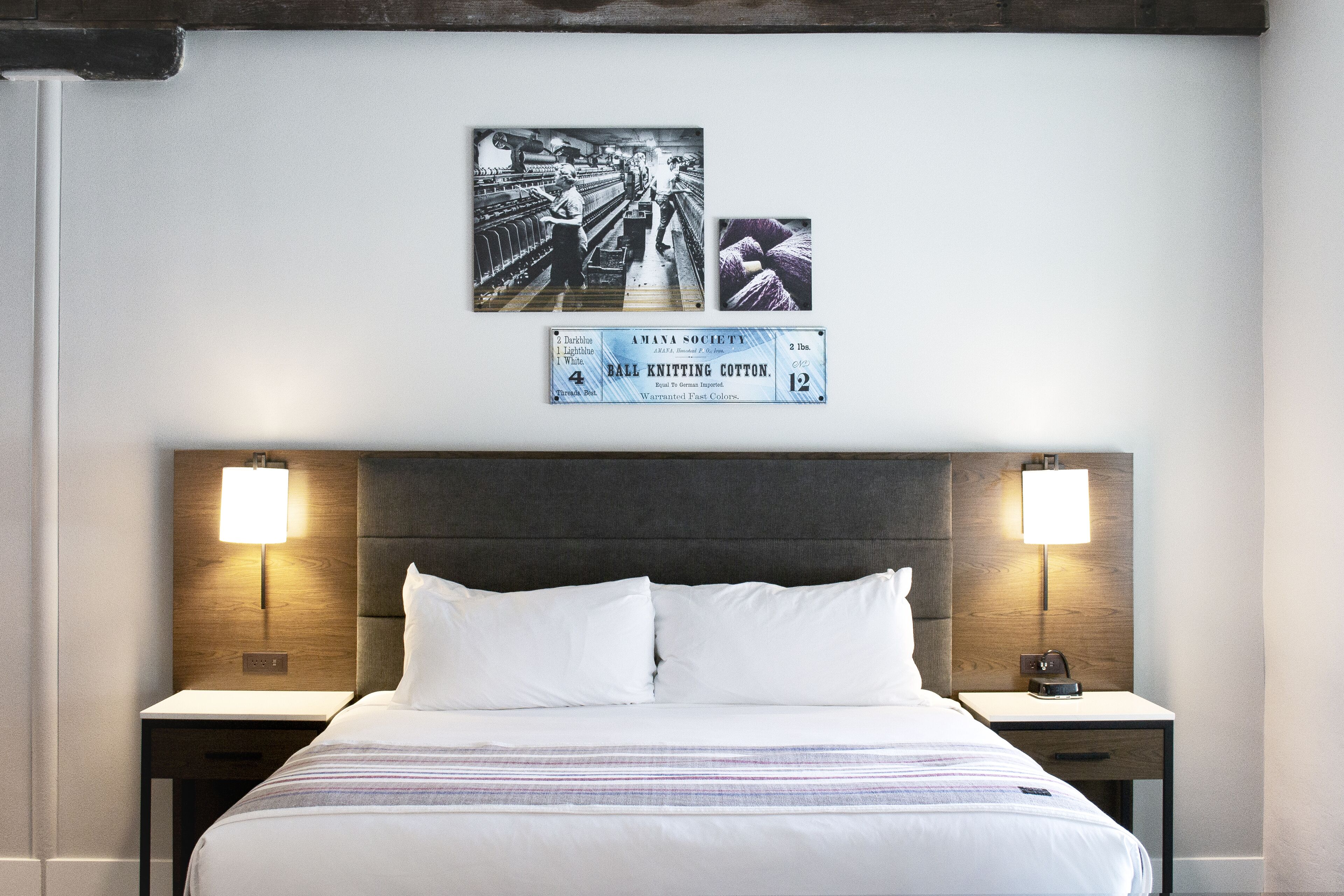 Ein Hotelzimmer mit einem großen Bett, zwei Nachttischen mit Lampen, einem hölzernen Kopfteil und Wandbildern mit Strickmotiven.