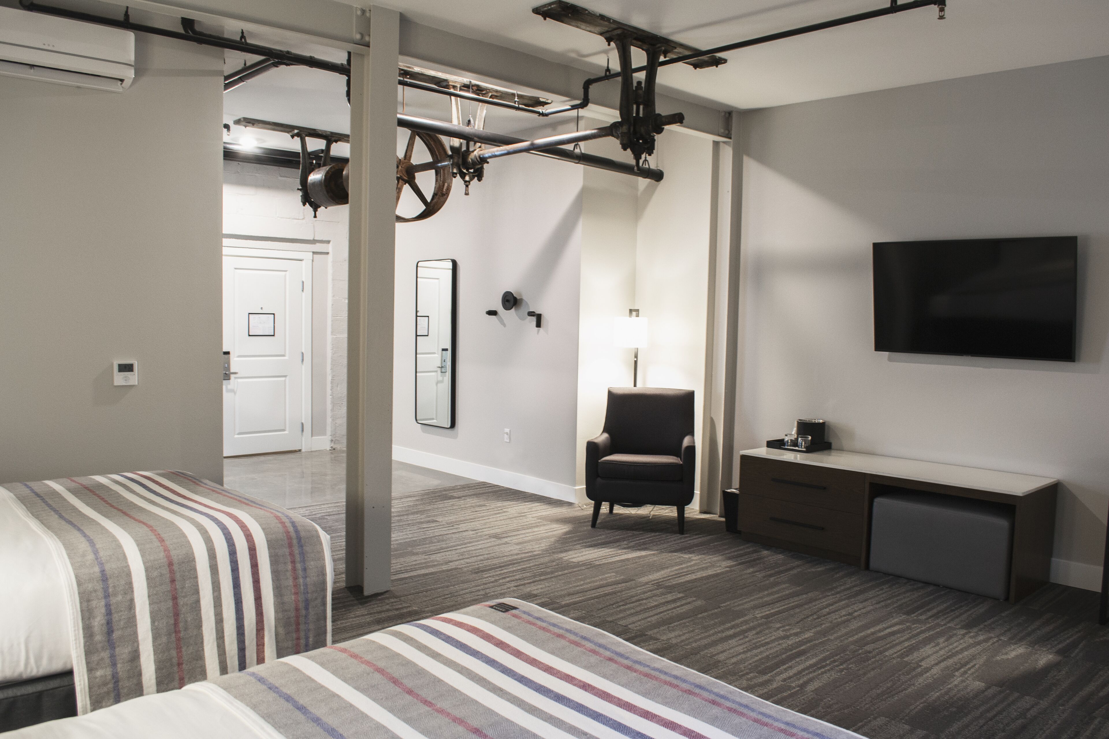 A hotel room with two beds, a desk, a chair, a TV, and a large mirror.