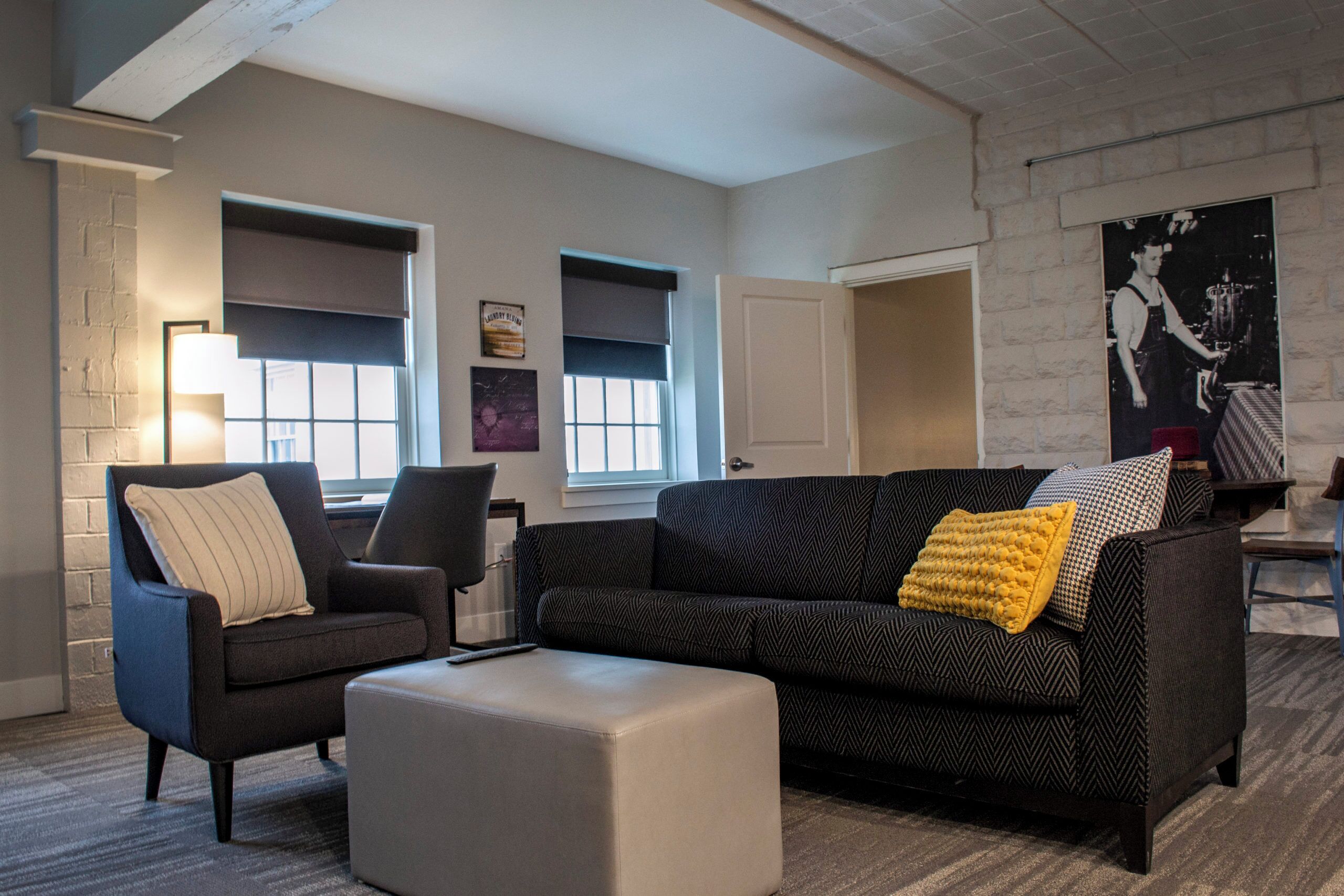 A living room with a sofa, armchair, ottoman, and a large window with blinds.