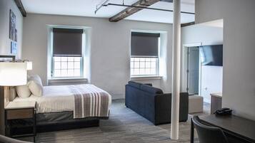 A modern hotel room with a bed, a sofa, a desk, and a TV.