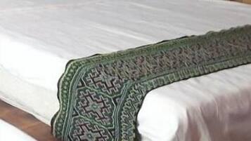 A bed with a wooden headboard, white bedding, and a patterned throw blanket.