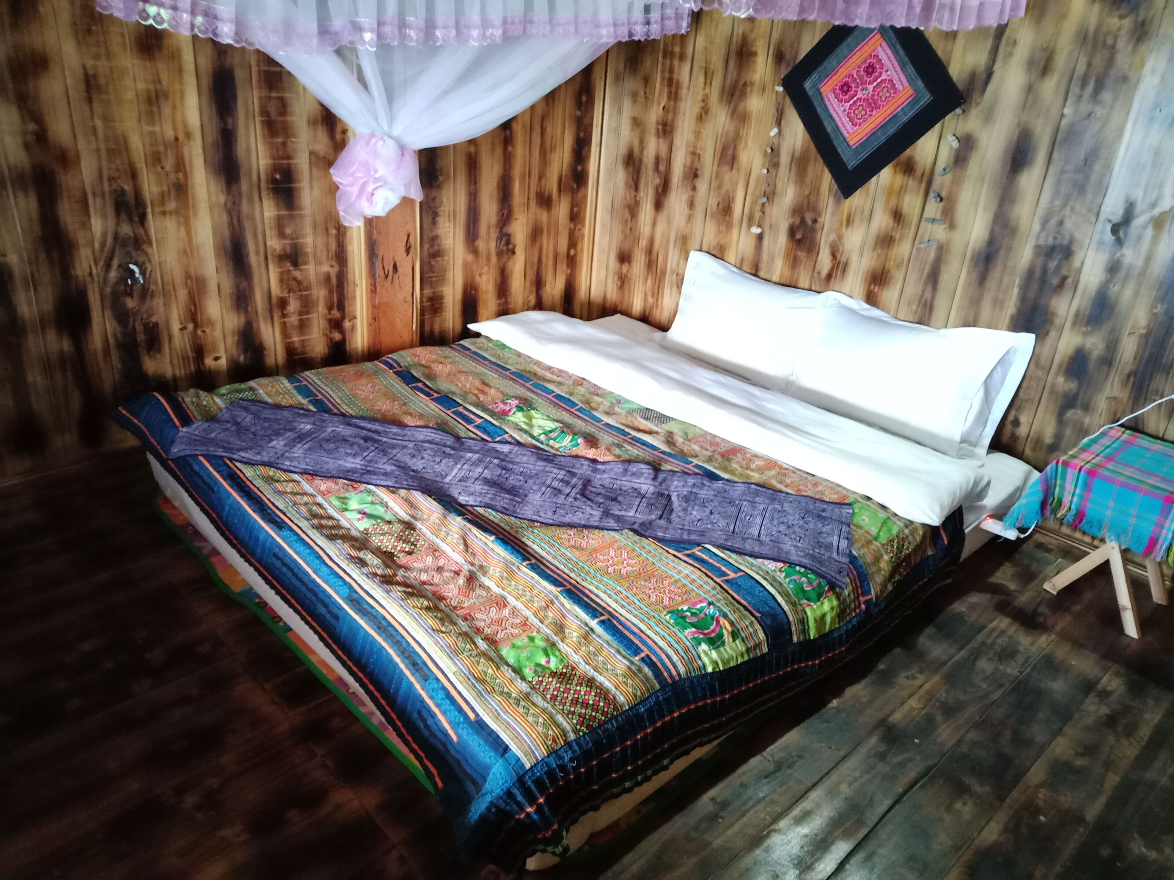 A wooden bed with a colorful blanket and a mosquito net.
