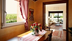 Un coin repas avec une table dressée pour deux personnes, un vase de fleurs et une vue sur le jardin par la fenêtre.