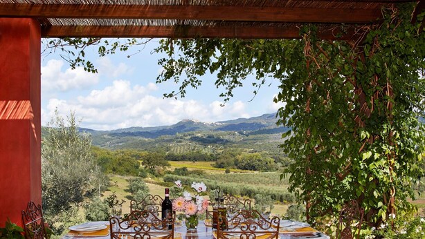 Un espace de restauration en plein air avec une table dressée pour quatre personnes, offrant une vue panoramique sur un paysage magnifique, avec des montagnes et des vignobles.