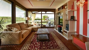 Un salon avec un canapé beige, une table basse à motifs et un tapis rouge et doré. On y trouve une bibliothèque agrémentée d’objets décoratifs et un mur d’accent rouge.