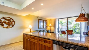 A modern kitchen with wooden cabinets, granite countertops, and a built-in dishwasher. - Aston Ka'anapali Shores 325 | Lush Garden Views – Pool, Hot Tub & Spa (Lahaina)