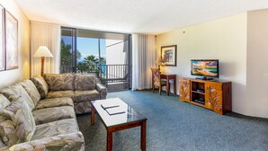 A living room with a sofa, a coffee table, a TV, and a balcony with curtains.