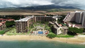 A resort with multiple buildings, a beach, and a mountainous backdrop.