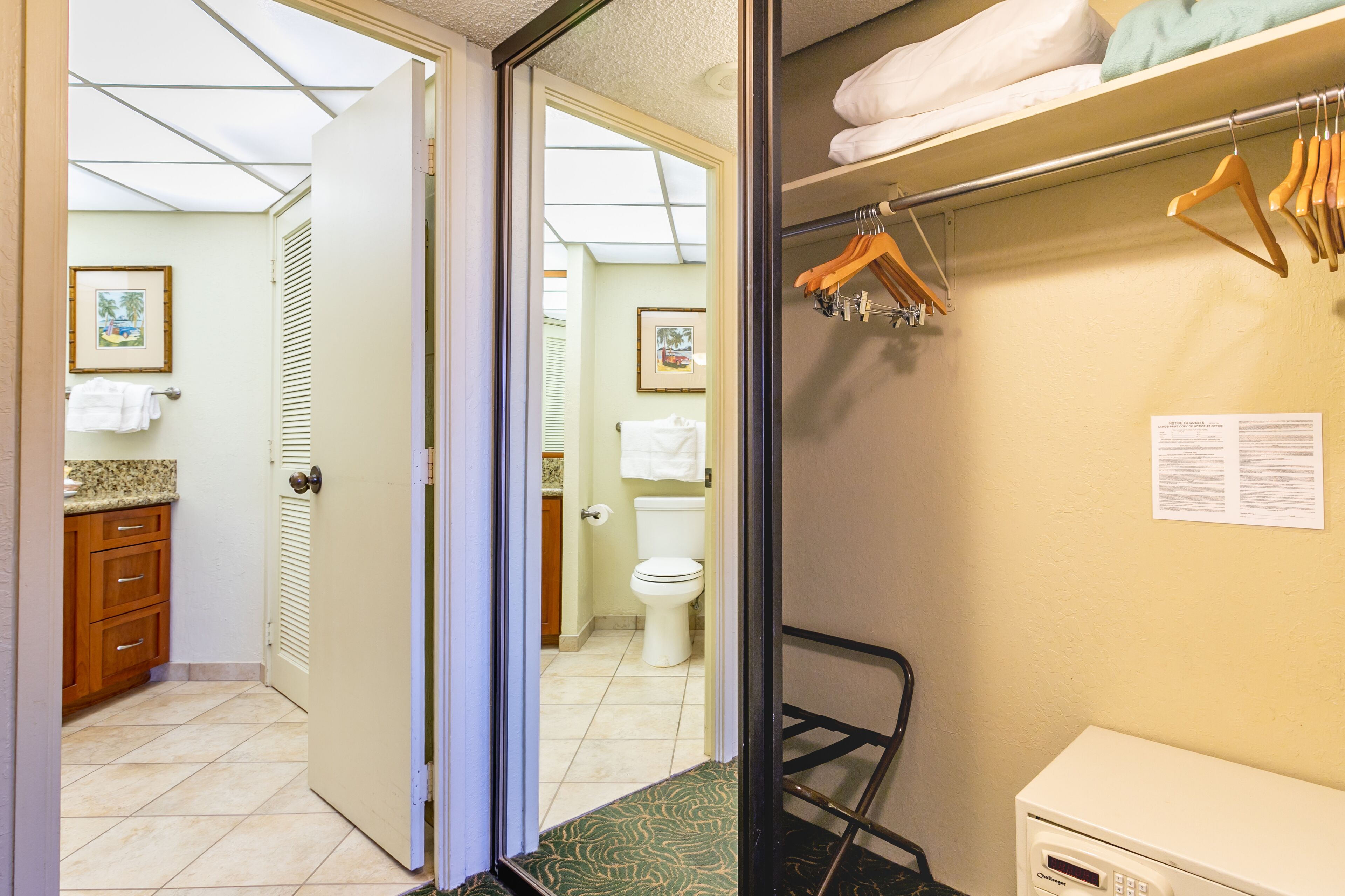 Une chambre d’hôtel avec salle de bain, un placard avec des vêtements suspendus et un avis affiché au mur.
