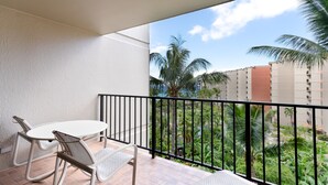 Un balcón con mesa y sillas blancas, barandilla negra y vistas a palmeras y edificios.