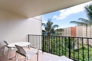 Ein Balkon mit weißem Tisch und Stühlen, einem schwarzen Geländer und Blick auf Palmen und Gebäude.