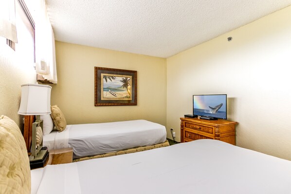 A hotel room with two beds, a television, a wooden dresser, and a framed picture on the wall.