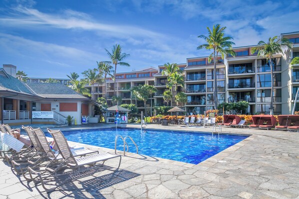 A hotel pool area with lounge chairs, a swimming pool, and a building with multiple balconies.