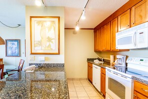 Una cocina con encimeras de granito, armarios de madera, microondas y estufa.