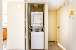 Lavanderia piccola e funzionale con lavatrice e asciugatrice, tubo di scarico e porta con cartello di sicurezza.