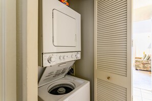 Máquina de lavar e secar empilhadas em lavanderia, com porta que dá para uma área de estar.