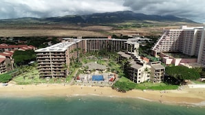 A resort with multiple buildings, a beach, and a mountainous backdrop.
