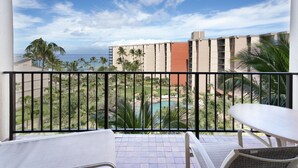 A balcony with a view of a pool, palm trees, and a building in the background.
