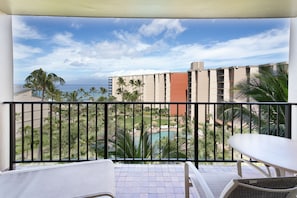 Un balcon avec vue sur une piscine, des palmiers et un bâtiment en arrière-plan.