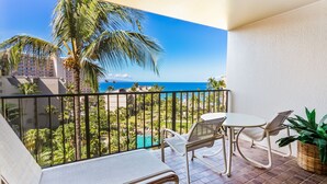 Ein Balkon mit Blick auf ein Schwimmbad und Palmen, inklusive Tisch mit Stühlen und einem Korbwäschekorb.