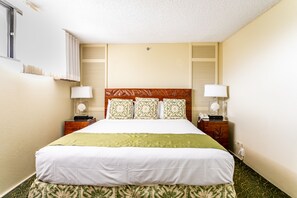 A hotel room with a large bed, two bedside tables with lamps, a wooden headboard, and a window with blinds.