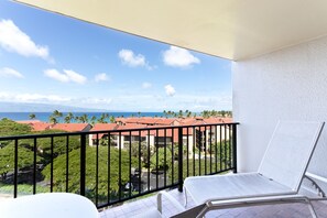 Ein Balkon mit weißem Stuhl, Blick auf ein Gebäude mit roten Dächern und einem klaren Himmel.