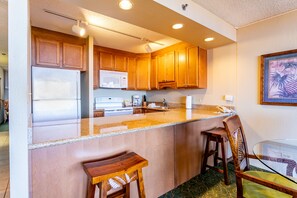 A kitchen with wooden cabinets, a stainless steel refrigerator, a microwave, and a glass island with bar stools.