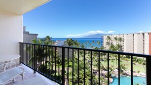 Un balcon avec vue sur une piscine, des palmiers et une montagne lointaine.