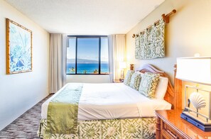 Een hotelkamer met een groot bed, uitzicht op zee, een houten hoofdeinde, een nachtkastje met een lamp en een decoratieve schelp.