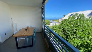 Un balcon avec une table et des chaises en bois, une vue sur la mer et une haie en arrière-plan.