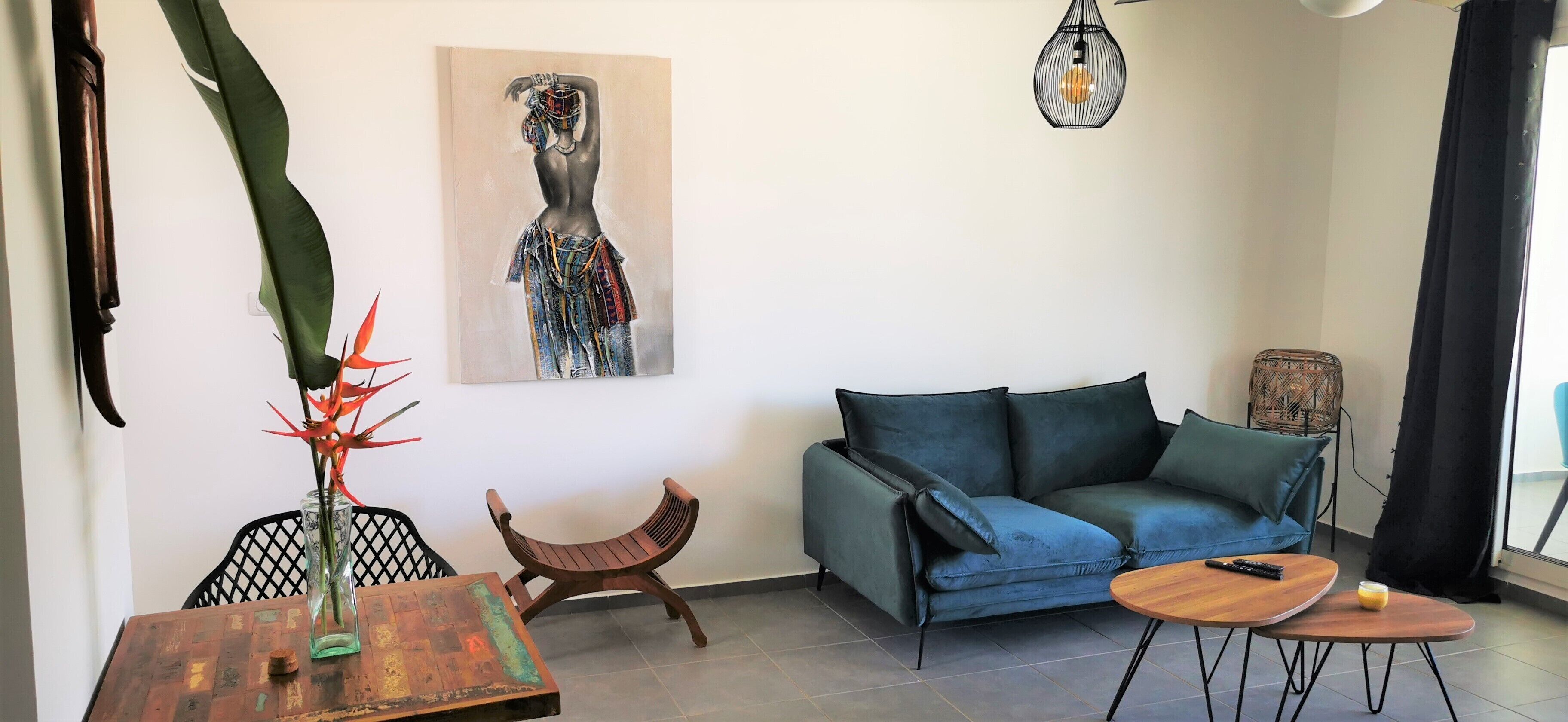 En moderne stue med en blå sofa, et træsofabord, et lille sidebord, en dekorativ stol, et billede på væggen og en hængende lampe.