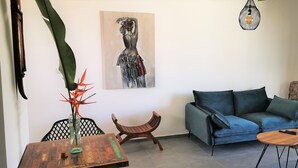 Un salon moderne avec un canapé bleu, une table basse en bois, une petite table d’appoint, un fauteuil décoratif, un tableau au mur et un luminaire suspendu.