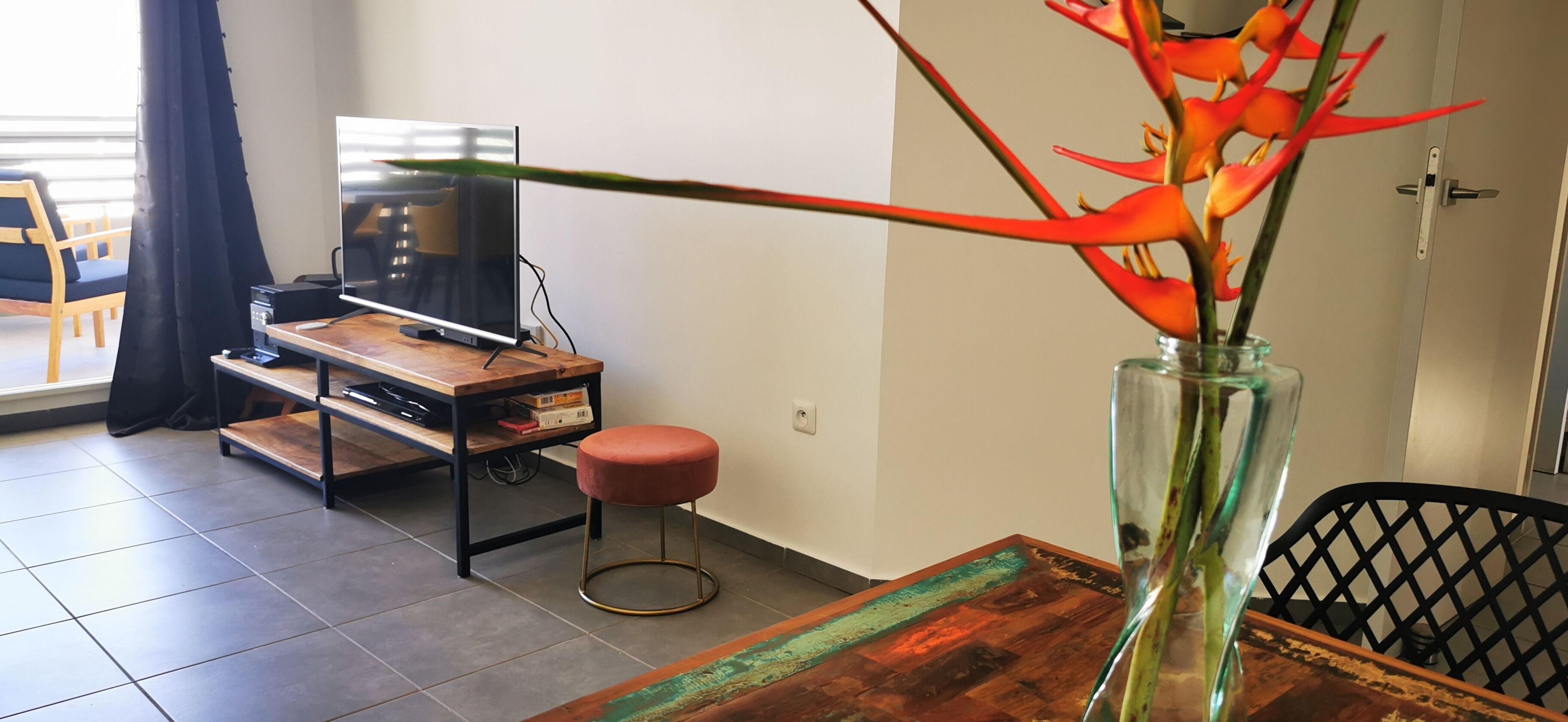 A modern living room with a wooden coffee table, a glass vase with a plant, a television, and a black chair.