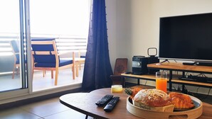 Une chambre d’hôtel équipée d’une télévision, d’une table en bois avec un petit-déjeuner, d’un meuble pour la télévision et offrant une vue sur le balcon extérieur.