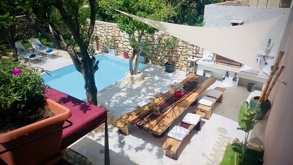 A poolside area with a stone wall, lounge chairs, and a wooden table with cushions.