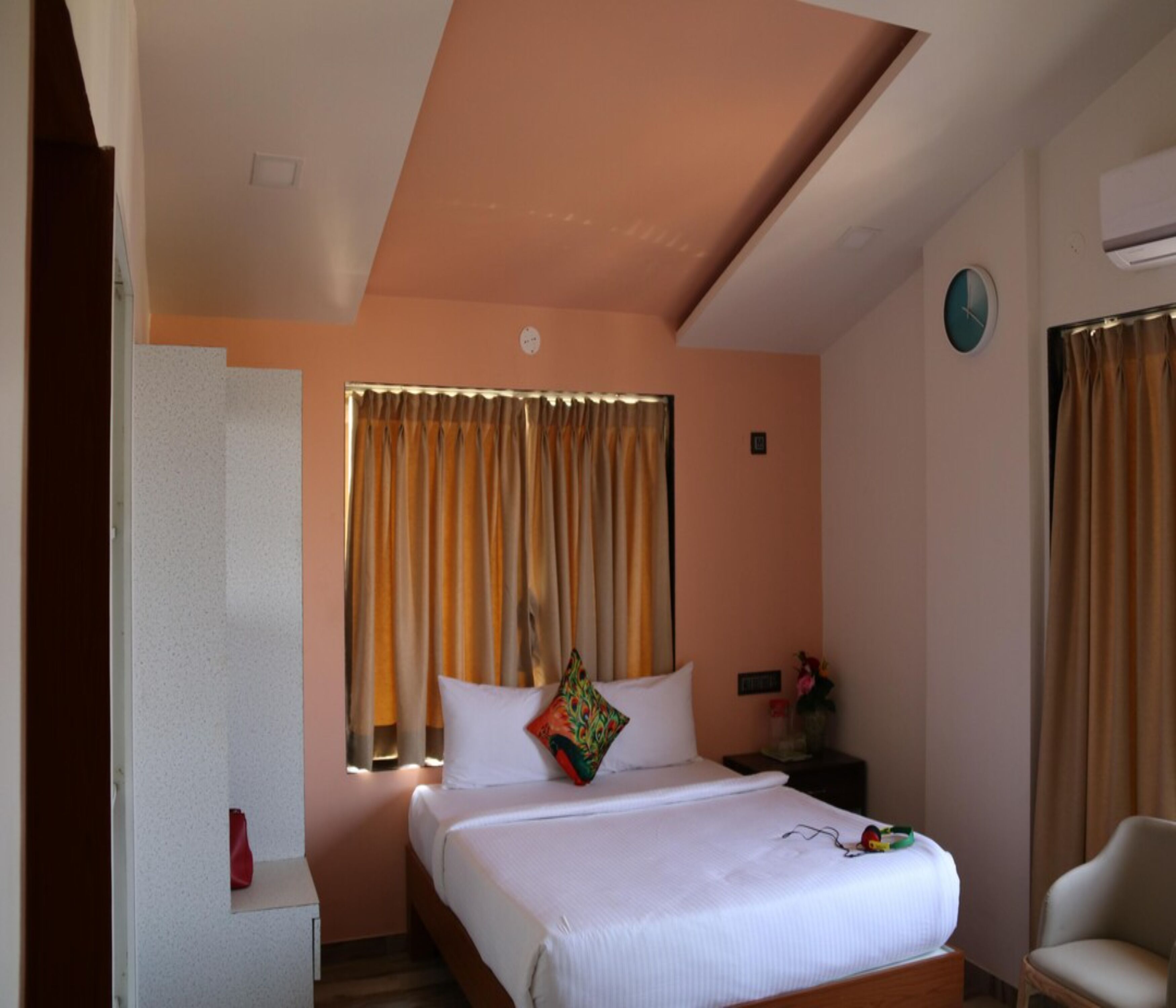 A hotel room with a bed, a chair, a nightstand, and a window with curtains.