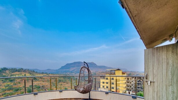 A balcony with a wooden floor, a hanging chair, and a view of a mountainous landscape.