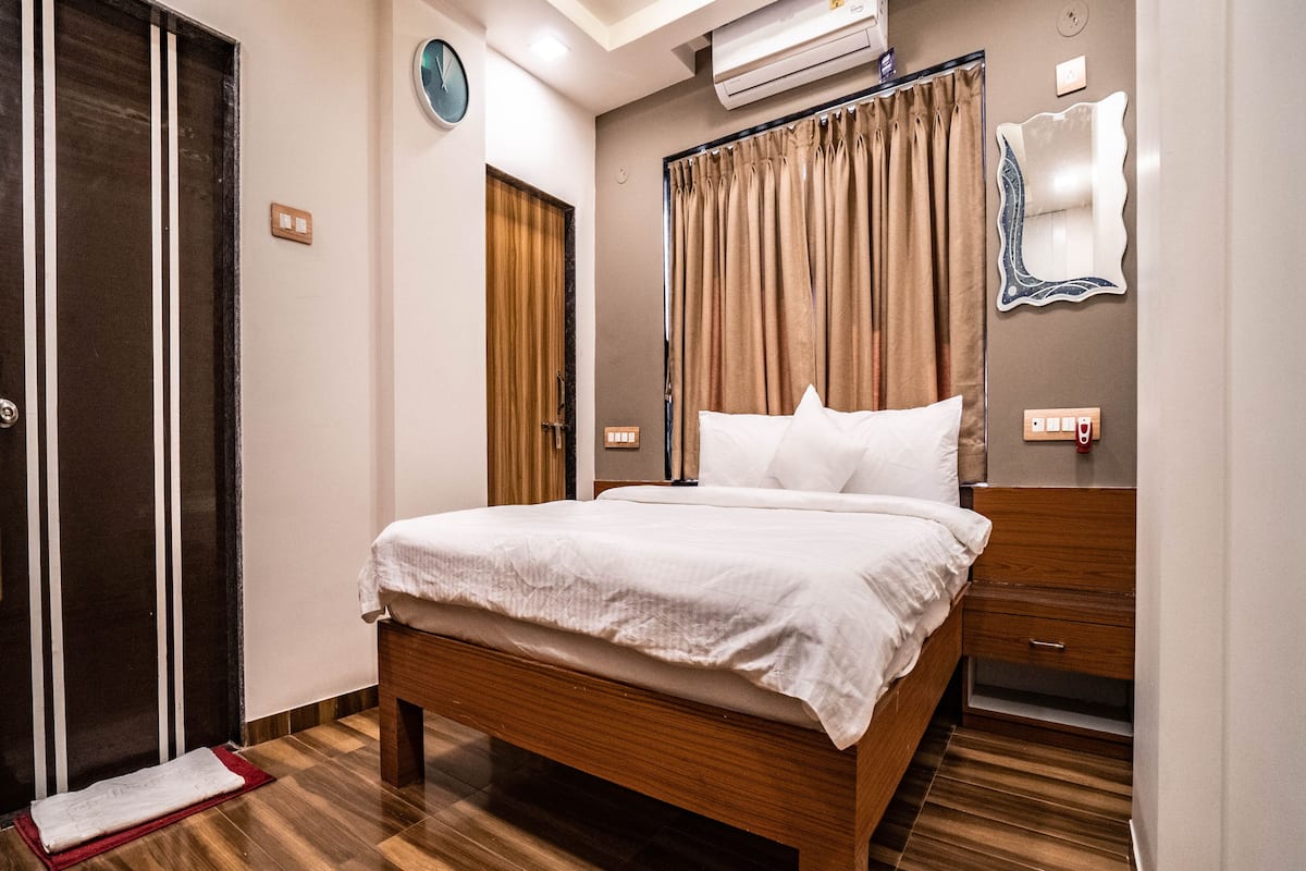 Une chambre d’hôtel avec un lit en bois, un tapis rouge, une table de chevet en bois, un miroir et un climatiseur fixé au mur.