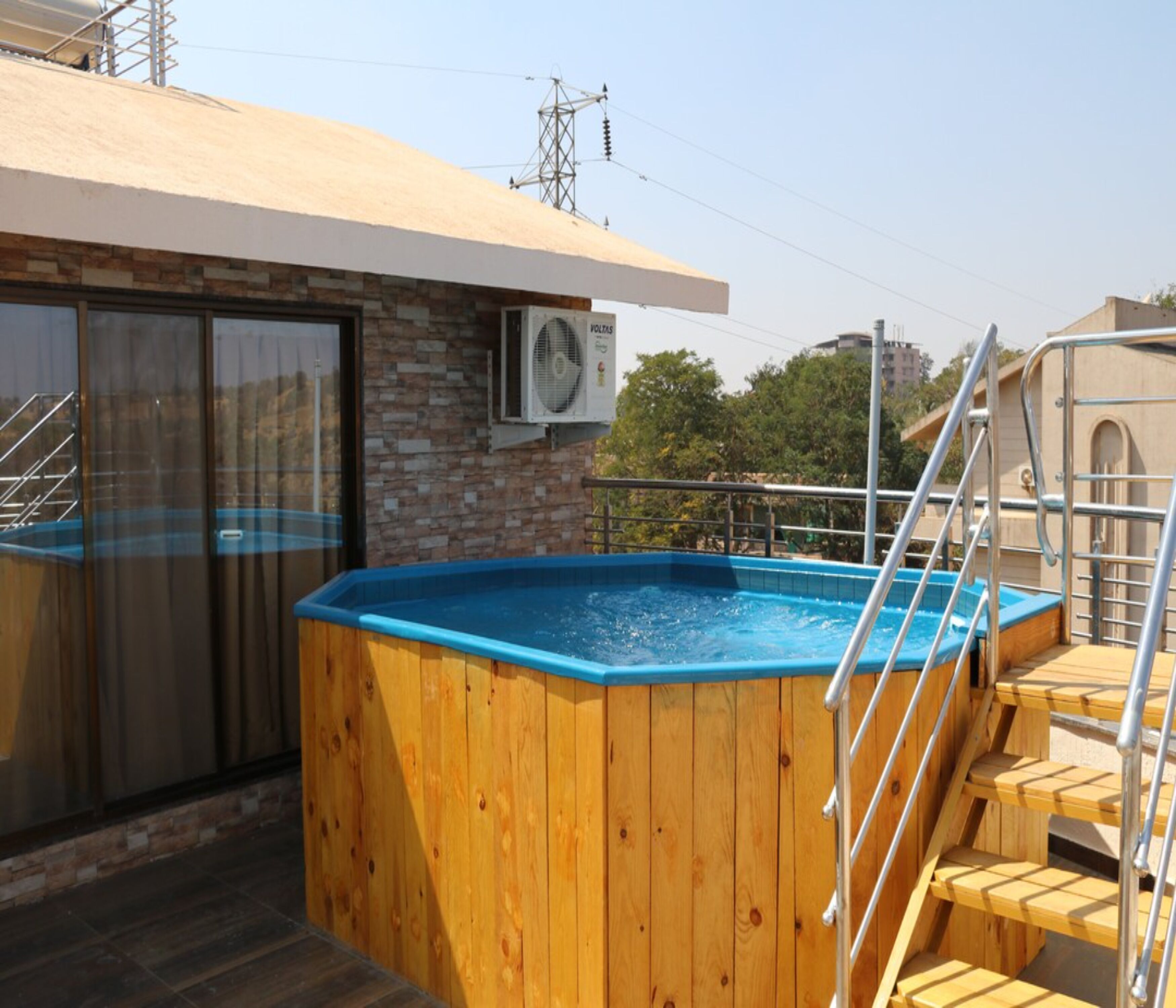 A wooden hot tub on a rooftop with a stone wall and a window.