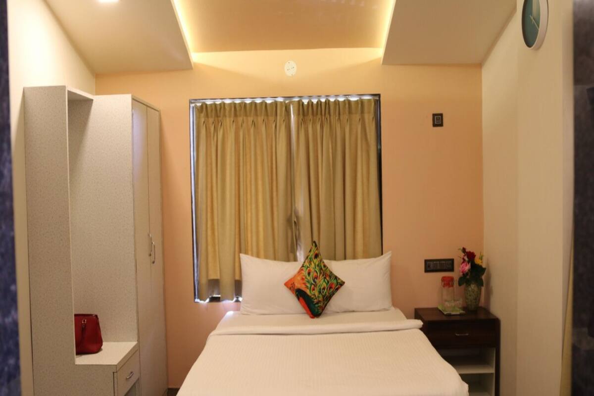 Une chambre d’hôtel comprenant un lit, une armoire, une table de chevet, une horloge et une fenêtre avec des rideaux.